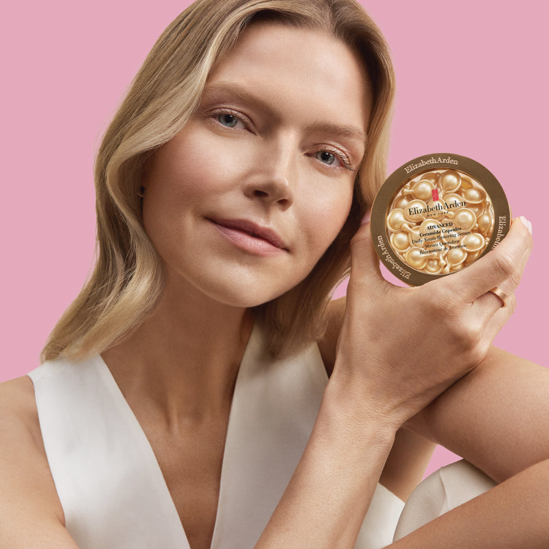 Woman holding Advanced Ceramide Daily Youth Capsules Serum product with a pink background