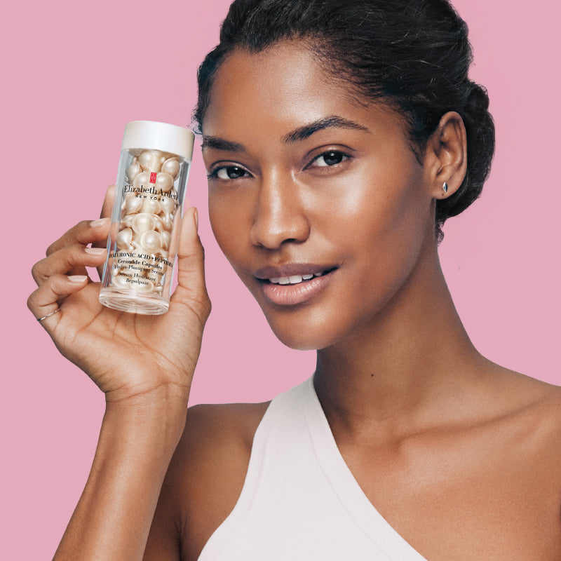 Woman holding Hyaluronic Acid + Peptides Capsules Serum skincare product against a pink background