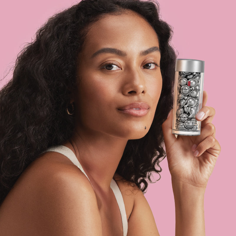 Woman holding Visible Brightening Capsules Serum against a pink background
