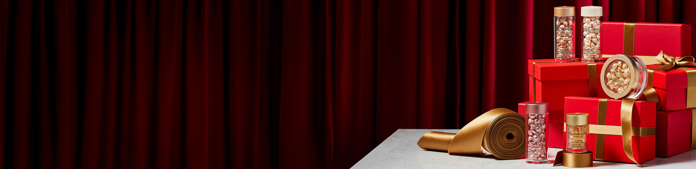 Elizabeth Arden Ceramide Capsules products on red gift boxes with gold ribbon featured along a deep red curtain back drop