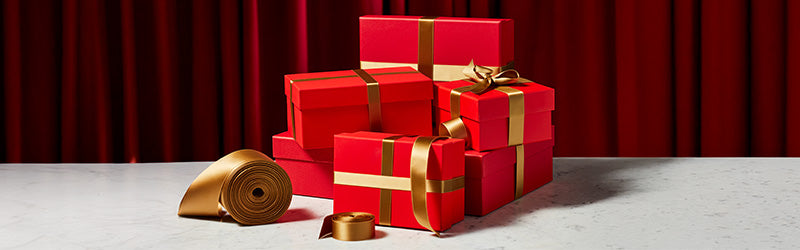Stack of red gift boxes with gold ribbons on a white surface with a red curtain background