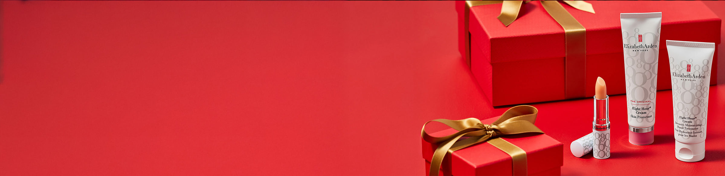 Red gift box with gold ribbon and Elizabeth Arden skincare products on a red background