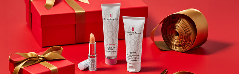 Red gift box with gold ribbon and Elizabeth Arden skincare products on a red background