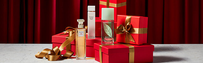 Perfume bottles sitting on red gift boxes with gold ribbon on a red curtain background
