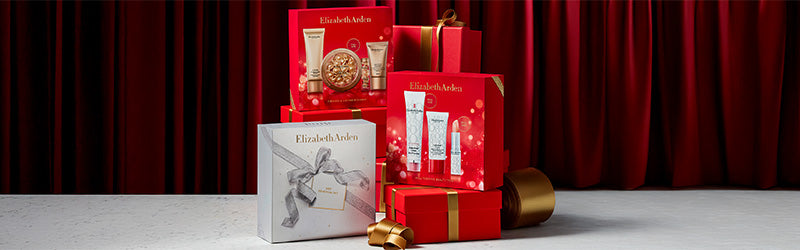 Elizabeth Arden gift sets featured on red gift boxes with gold ribbon on a red curtain background