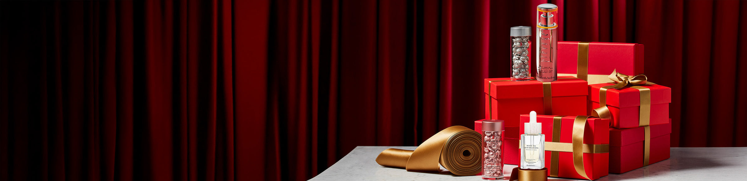 Elizabeth Arden Skin care products on red gift boxes with gold ribbon featured along a deep red curtain back drop