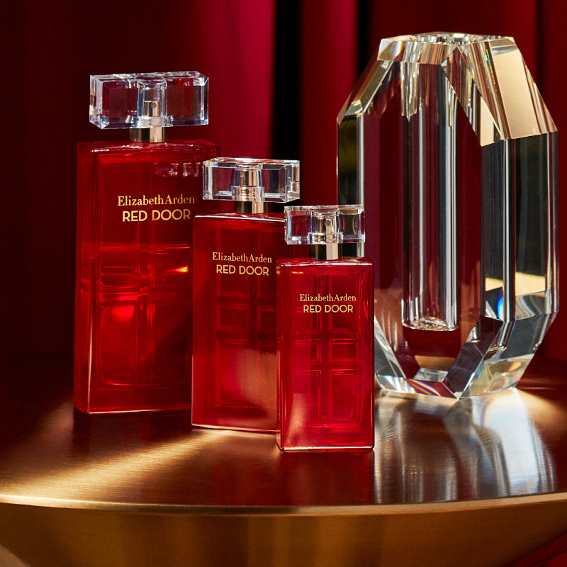 Elizabeth Arden Red Door perfume bottles on a reflective surface with a red background