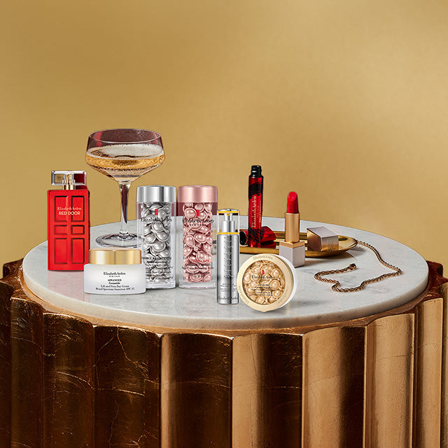 Tabletop display with beauty products, jewelry, and a glass of champagne on a gold background