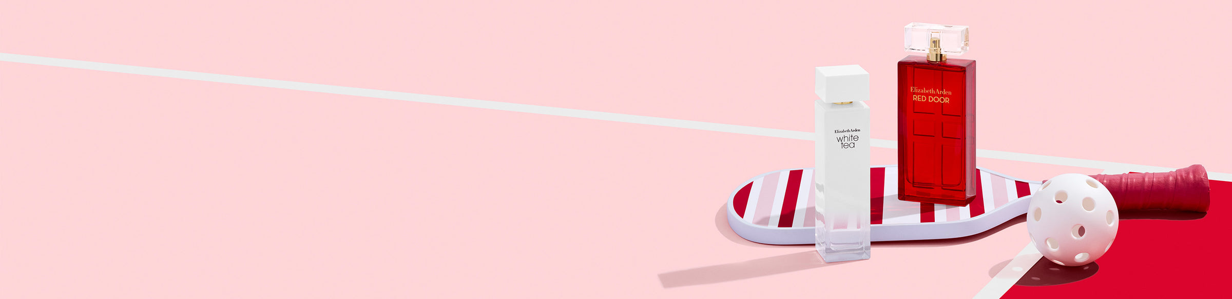 Two perfume bottles on stripe pickleball paddle on a pink and red background next to a ball