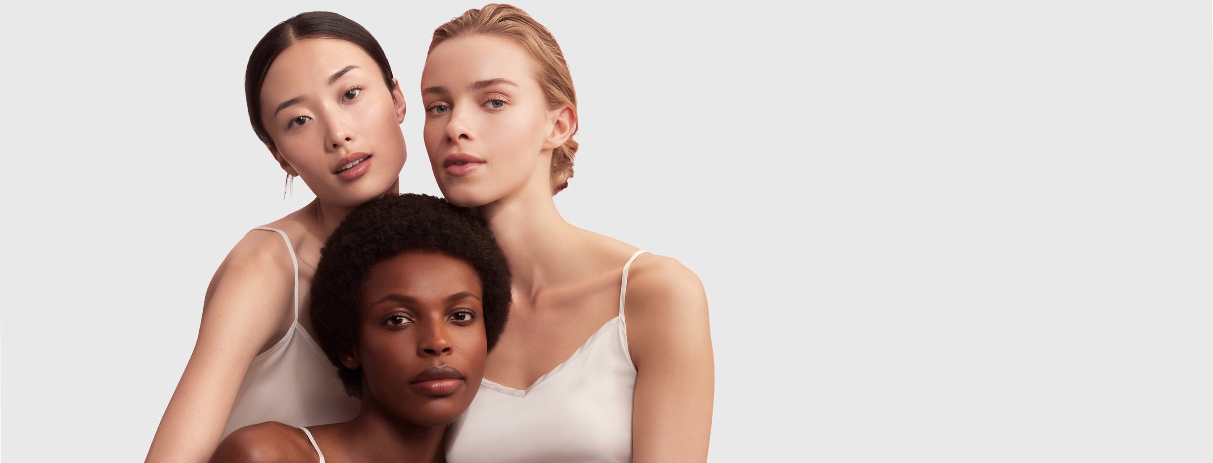 Three women wearing white tank tops against a light gray background