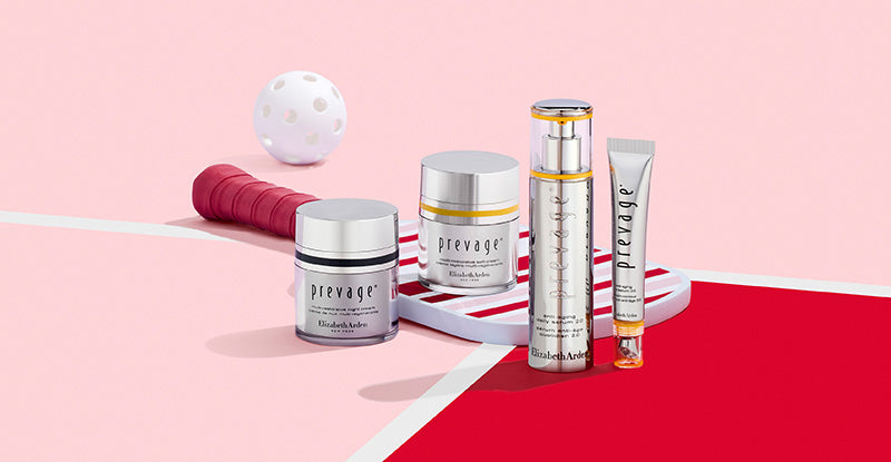 Collection of Prevage skincare products on a stripe pickleball paddle on a pink and red background next to a call