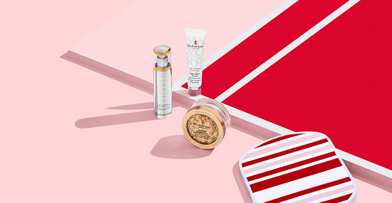 Collection of Elizabeth Arden products on a pink and red background next to a stripe pickleball paddle