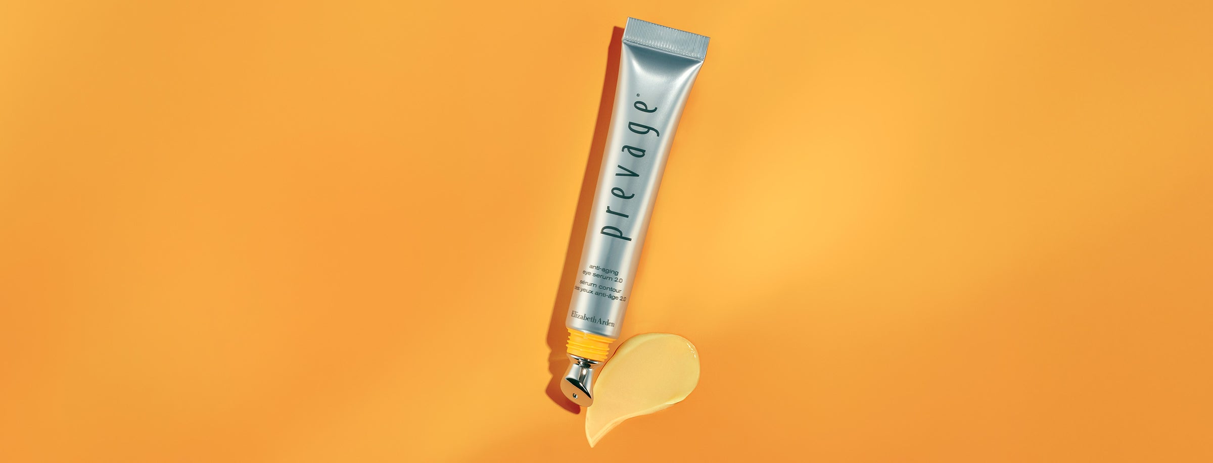 Prevage skincare tube with applicator and spill of product on an orange background