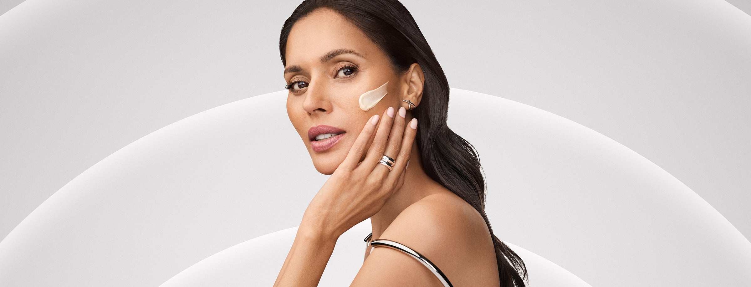 Woman applying cream to her face with a neutral background