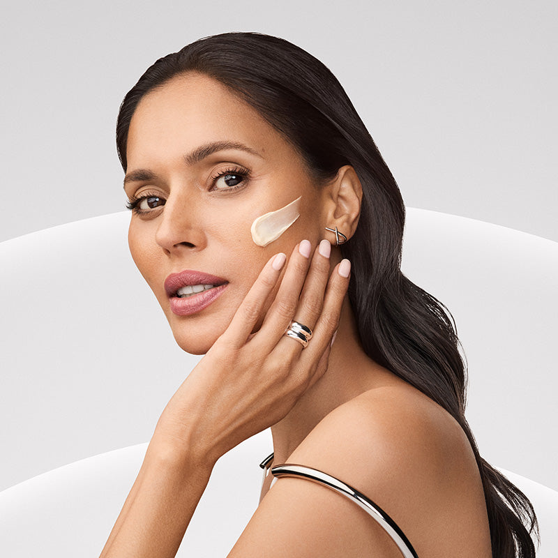 Woman applying cream to her face with a neutral background