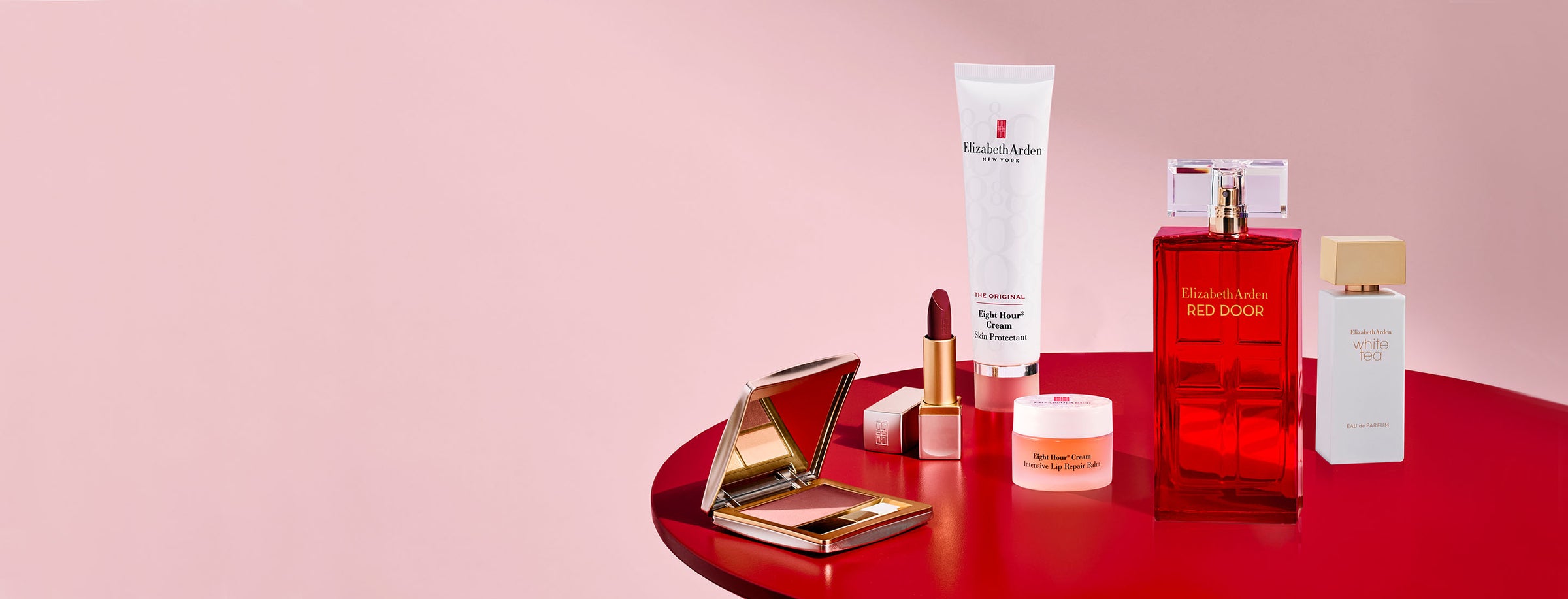 Collection of Elizabeth Arden beauty products on a red platform with a pink background