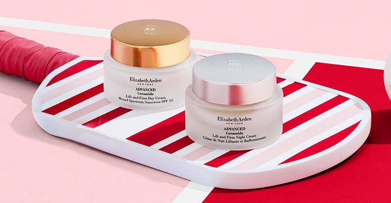 Two skincare jars on a white tray with a pink and red striped background