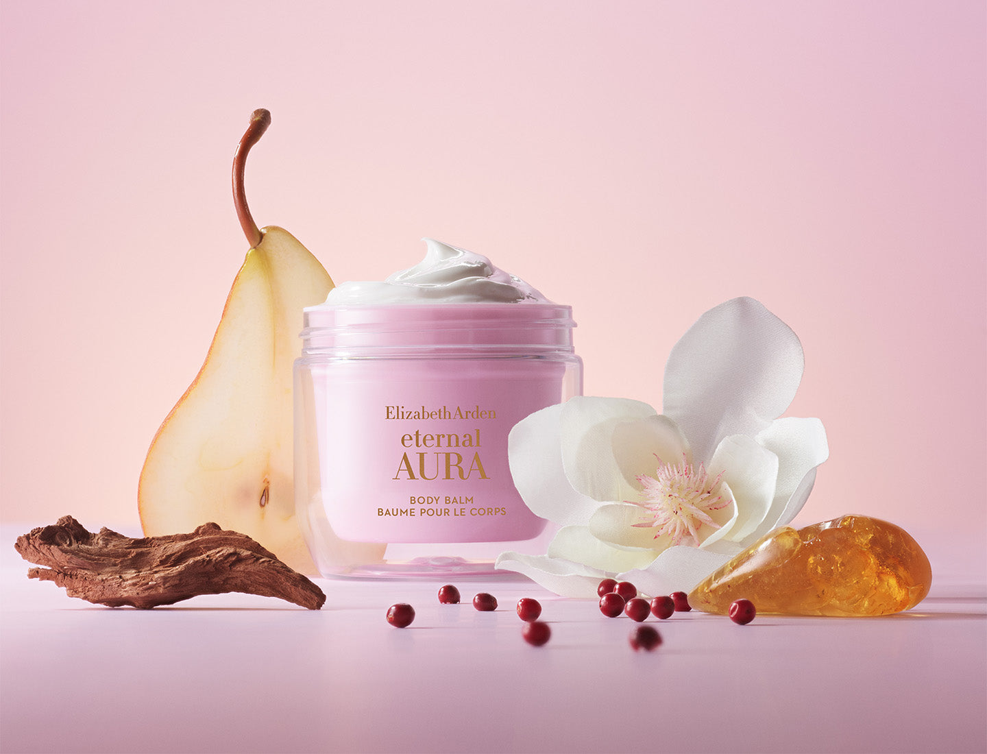 Elizabeth Arden Eternal Aura body balm with a golden pear, white magnolia flower, sandalwood, pink pepper and honeycomb on a pink background