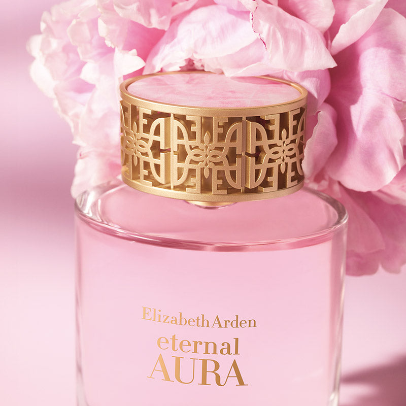Pink Elizabeth Arden Eternal Aura perfume bottle with gold cap against a pink floral background