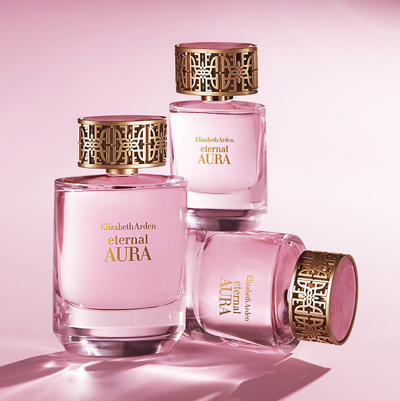 Three bottles of Elizabeth Arden Eternal Aura perfume on a pink background