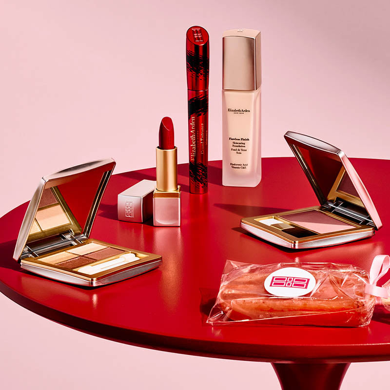Makeup products including a compact, lipstick, and foundation on a red surface with a pink background
