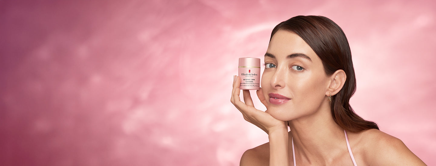 Woman holding a jar of Elizabeth Arden eye cream against a pink background