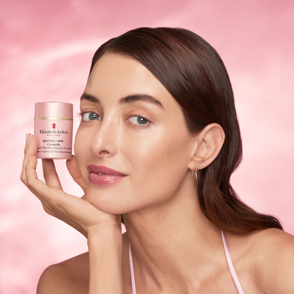 Woman holding a jar of Elizabeth Arden eye cream against a pink background