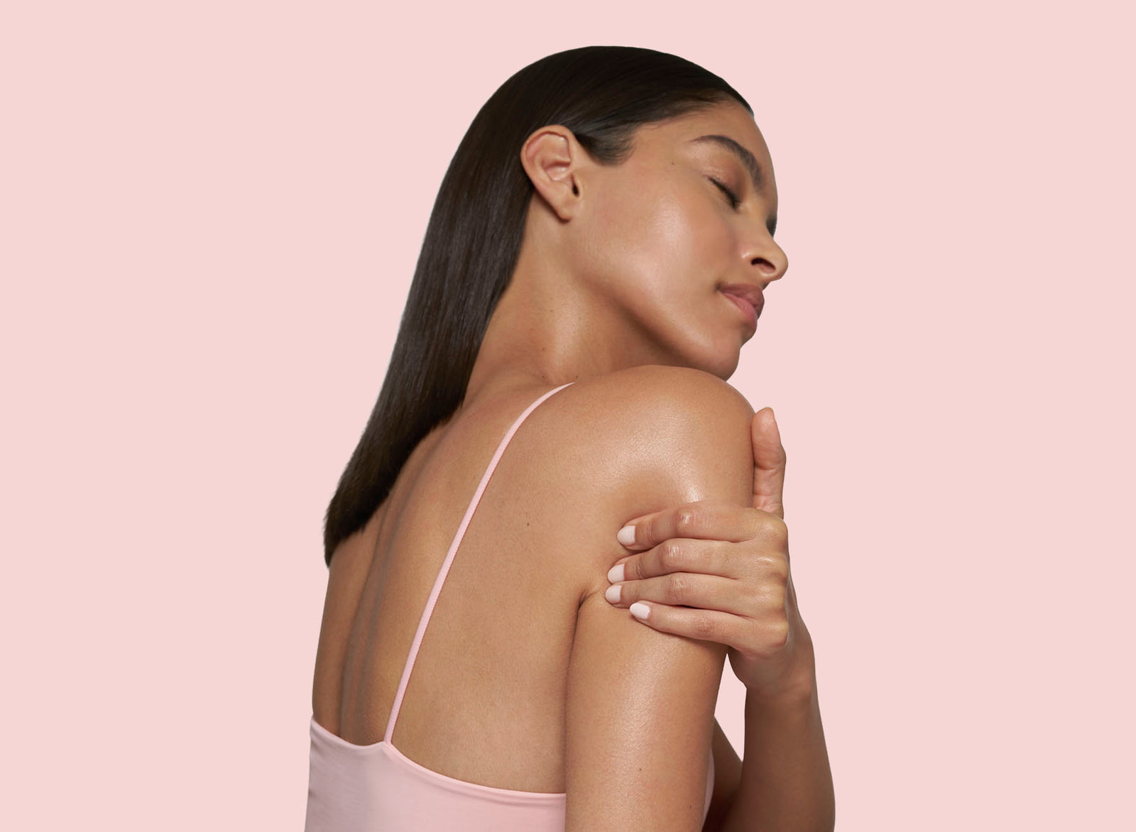 Woman with long dark hair wearing a pink strappy top against a light pink background
