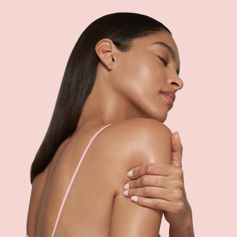 Woman with long dark hair wearing a pink strappy top against a light pink background