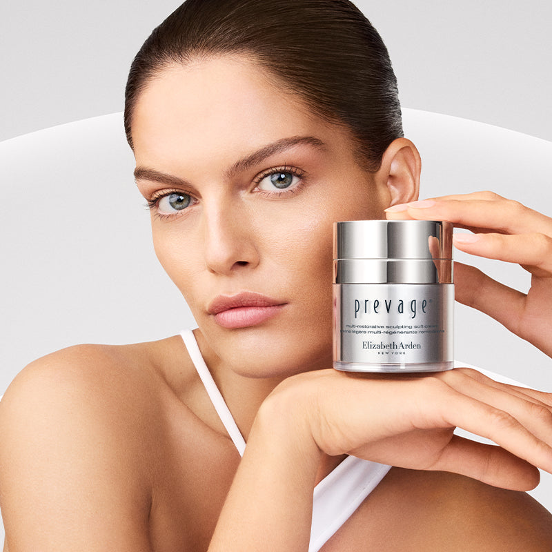 Woman holding a jar of Elizabeth Arden Prevage cream against a neutral background