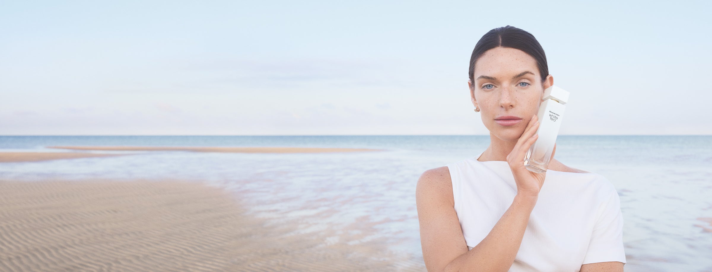 Woman holding a white tea fragrance on a beach with a clear sky