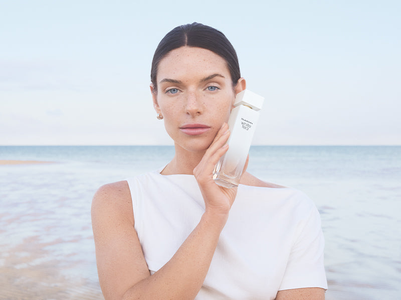 Woman holding a white tea fragrance on a beach with a clear sky