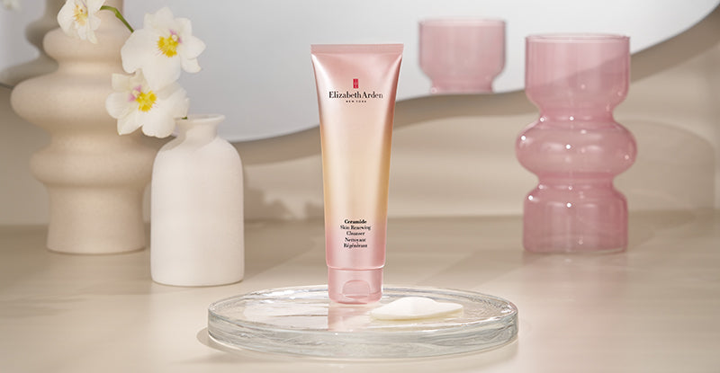 Elizabeth Arden Ceramide Cleanser on a clear tray against a beige background next to 2 vase with flowers.