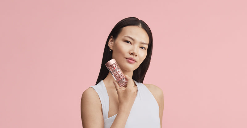 Woman holding bottle of capsules against a pink background