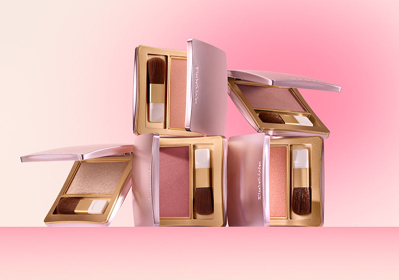 Makeup products including blushes and brushes on a pink background