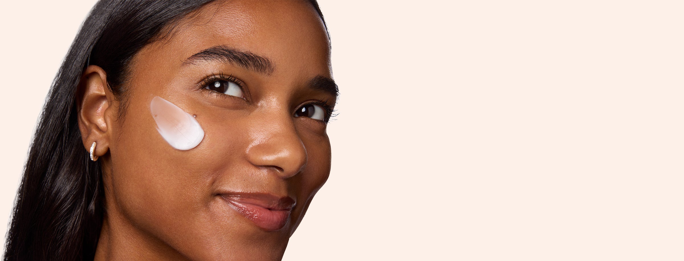 Woman with a skincare product on her face against a beige background
