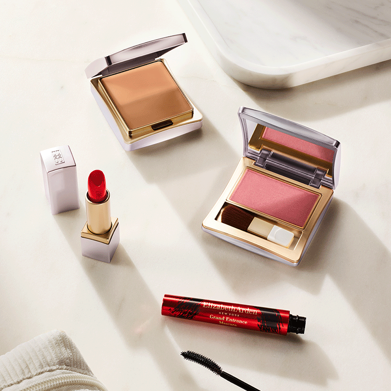 Makeup products including a lipstick, blush, and mascara on a light surface.

