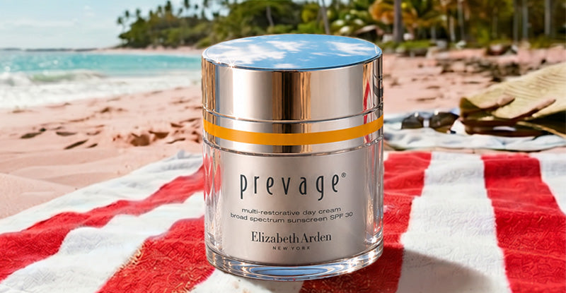 Prevage skincare cream jar on a beach towel with ocean and palm trees in the background