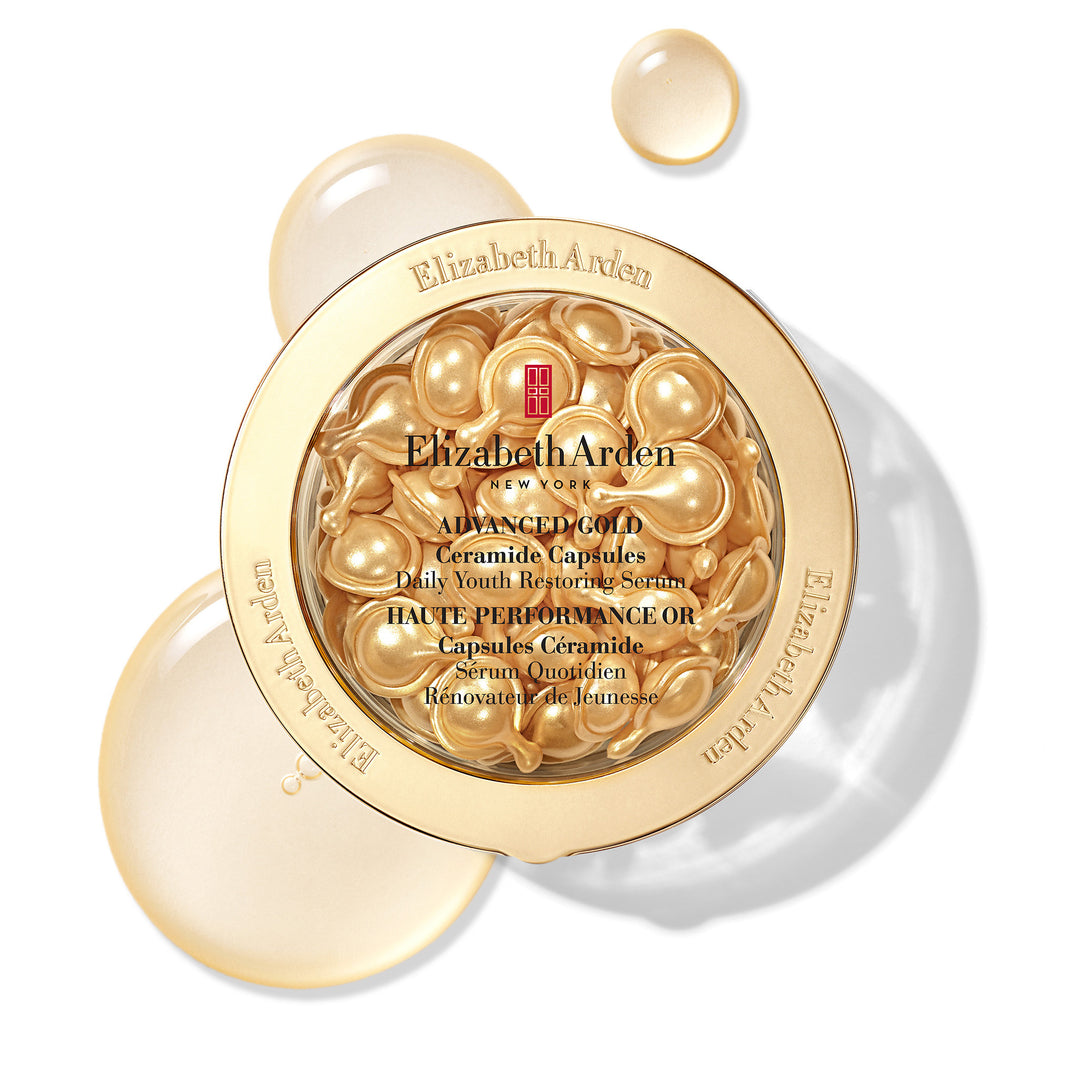 Elizabeth Arden Advanced Gold Ceramide Capsules in a round gold container with the lid removed, showing the golden capsules inside, on a white background with decorative golden liquid droplets.