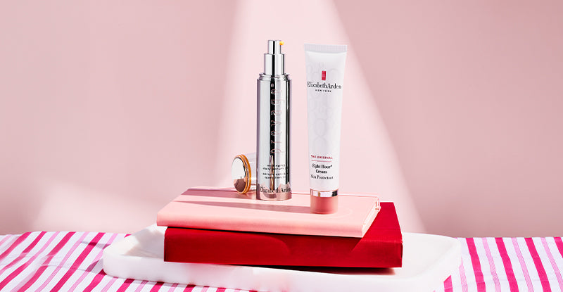 Elizabeth Arden Prevage Anti-aging 2.0 serum and Eight Hour Skin Protectant sitting on top of books on a pink background. 