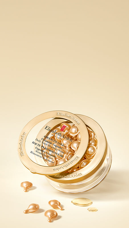 Elizabeth Arden Advanced Gold Ceramide Capsules Daily Youth Restoring Serum in a clear jar with a gold lid, shown on a warm beige background with a few capsules and texture spill scattered in front.