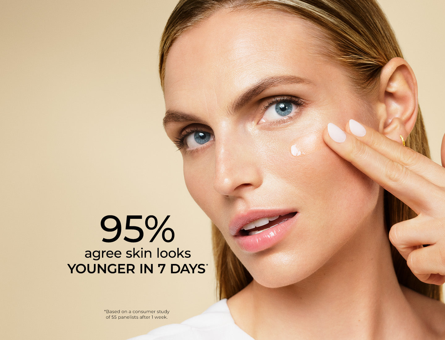 Close-up of a woman with blue eyes applying a skincare droplet to her cheek against a warm beige background, with text reading '95% agree skin looks YOUNGER IN 7 DAYS'.