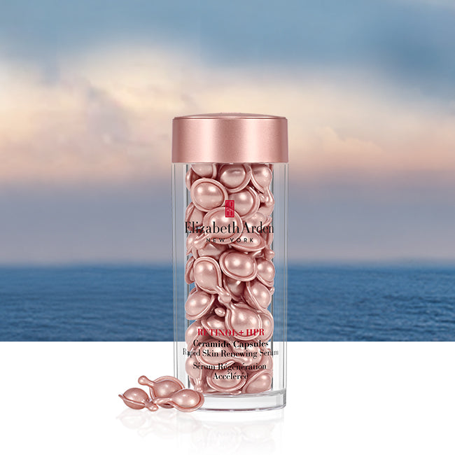 Elizabeth Arden Retinol + HPR Ceramide Capsules in a clear cylindrical bottle with a metallic rose gold cap, set against a scenic ocean and sky background.