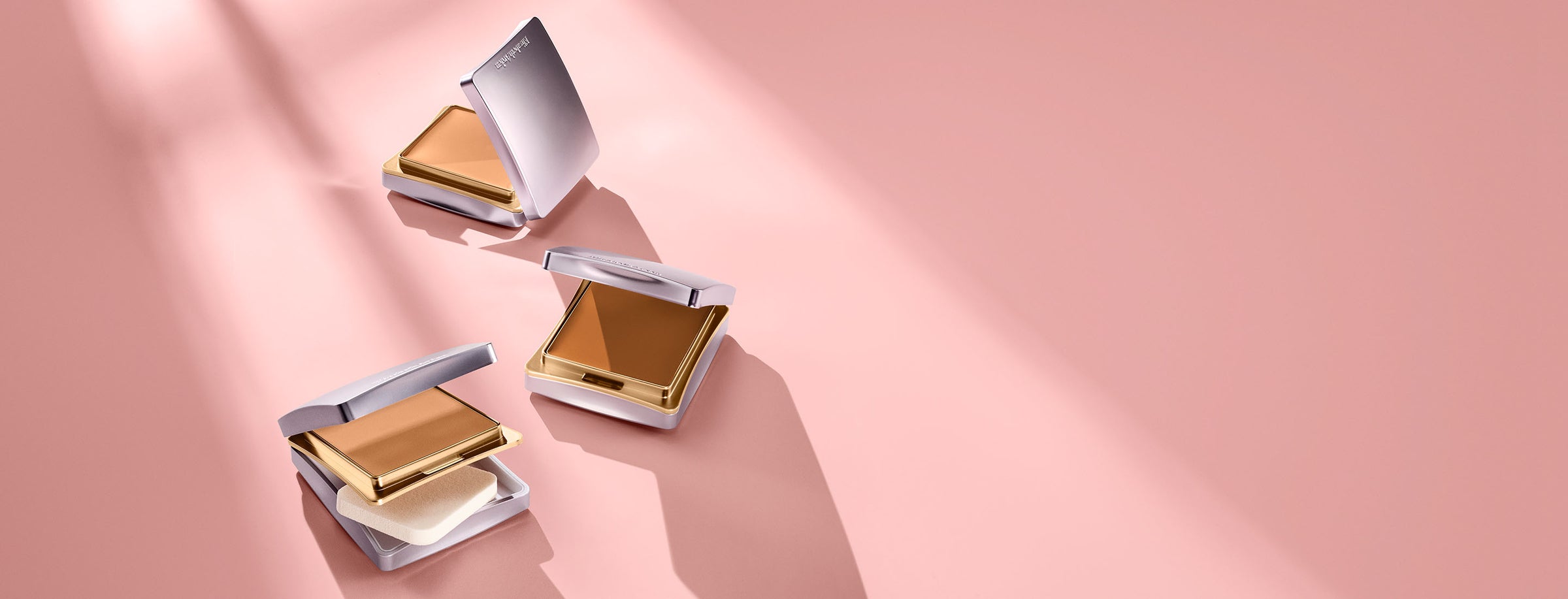 Three compact powder cases on a pink background