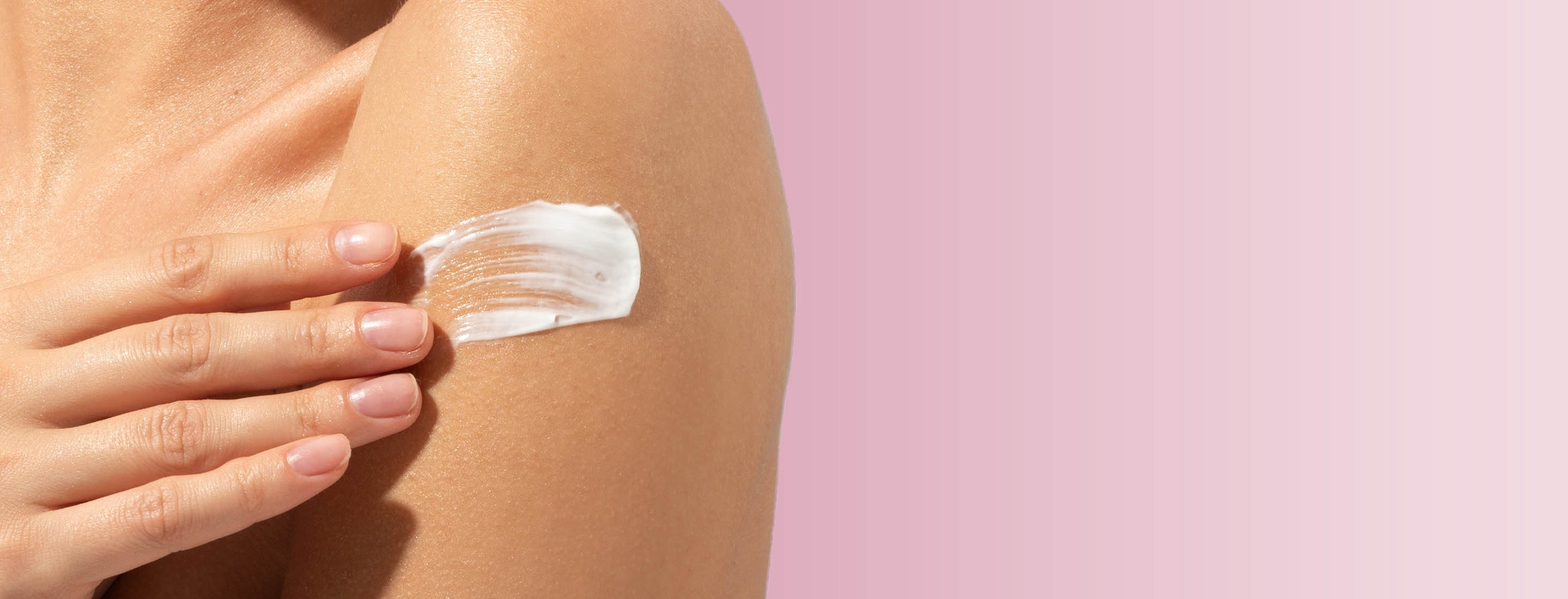 Hand applying Eternal Aura body balm to a shoulder with a pink background for desktop