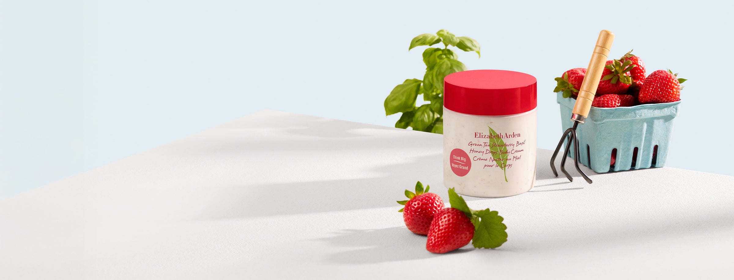 Jar of Green Tea Strawberry Basil Honey Drops Body Cream with strawberries in a basket on a white surface