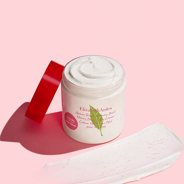 Green Tea Strawberry Basil Honey Drops Body Cream jar with a swatch on a pink background.