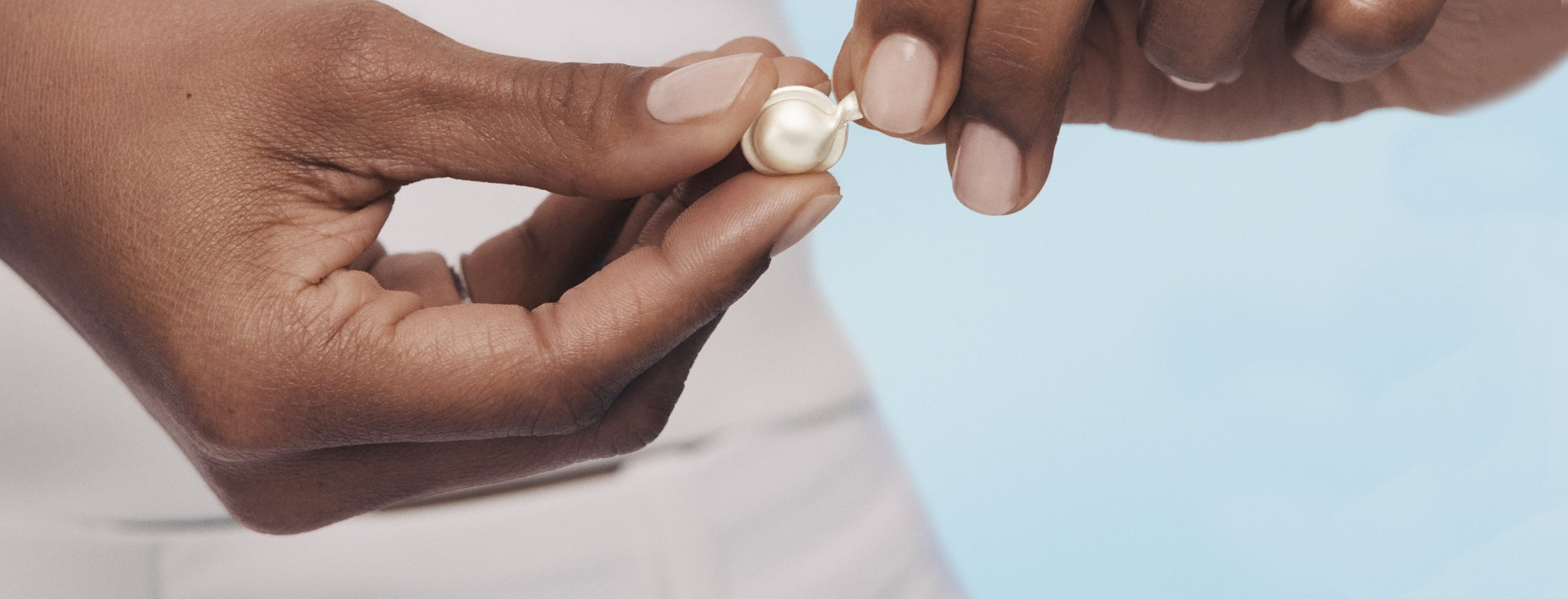Close-up of hands holding a Hyaluronic Acid + Peptide Capsule against a light blue background