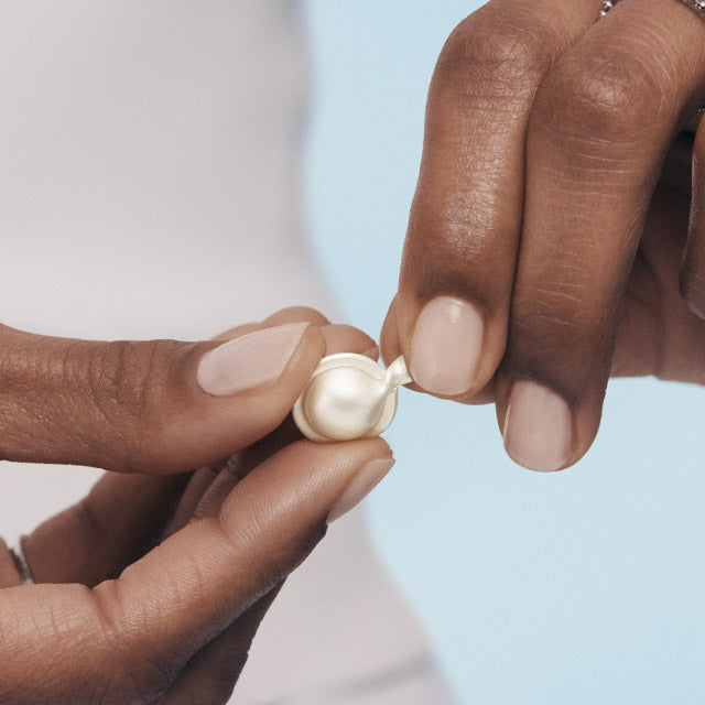 Close-up of hands twisting a Hyaluronic Acid + Peptide Capsule against a light blue background