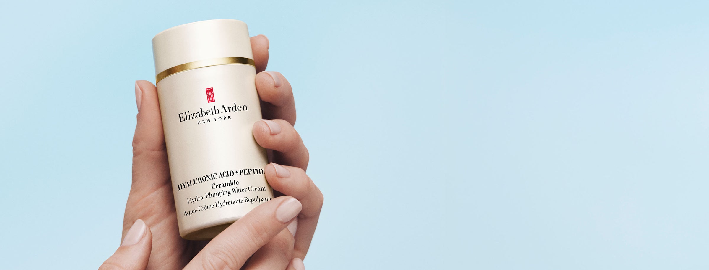 Hand holding a bottle of Elizabeth Arden Hyaluronic Acid + Peptides Water cream against a light blue background
